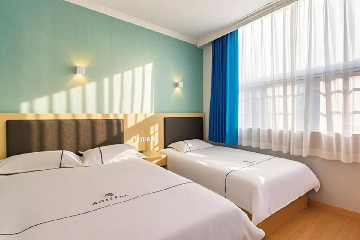 A hotel room with two beds, a wooden headboard, a nightstand, and a window with curtains.