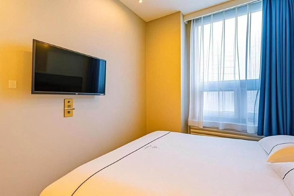 Quarto de hotel com cama, televisão na parede e janela com cortinas.