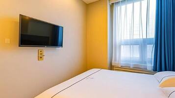 Quarto de hotel com cama, televisão na parede e janela com cortinas.