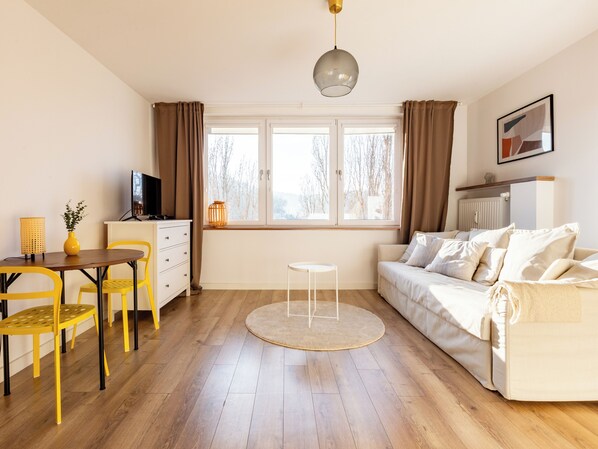 Un salon moderne comprenant un canapé, un téléviseur, une table à manger avec des chaises, un petit tapis rond et une fenêtre avec des rideaux.