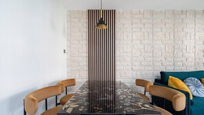 A dining area with a table and chairs, a patterned tablecloth, a wall with a brick-like texture, and a sofa with cushions.