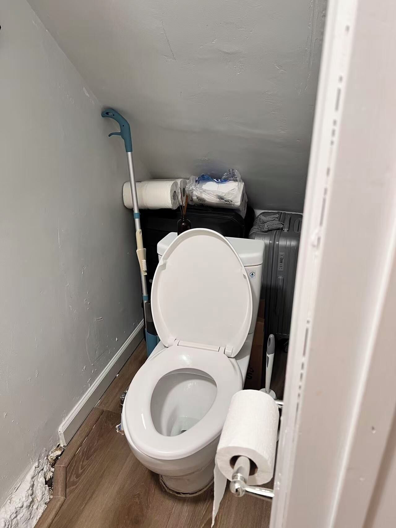 Une petite salle de bain compacte, équipée de toilettes, d’un rouleau de papier toilette et d’une serpillière.