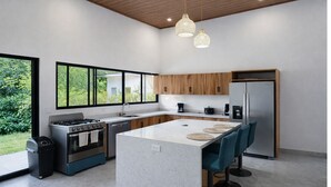 A modern kitchen with a central island, wooden cabinets, stainless steel appliances, and large windows. - Private Pool Oasis Near Ballena National Park (Uvita)