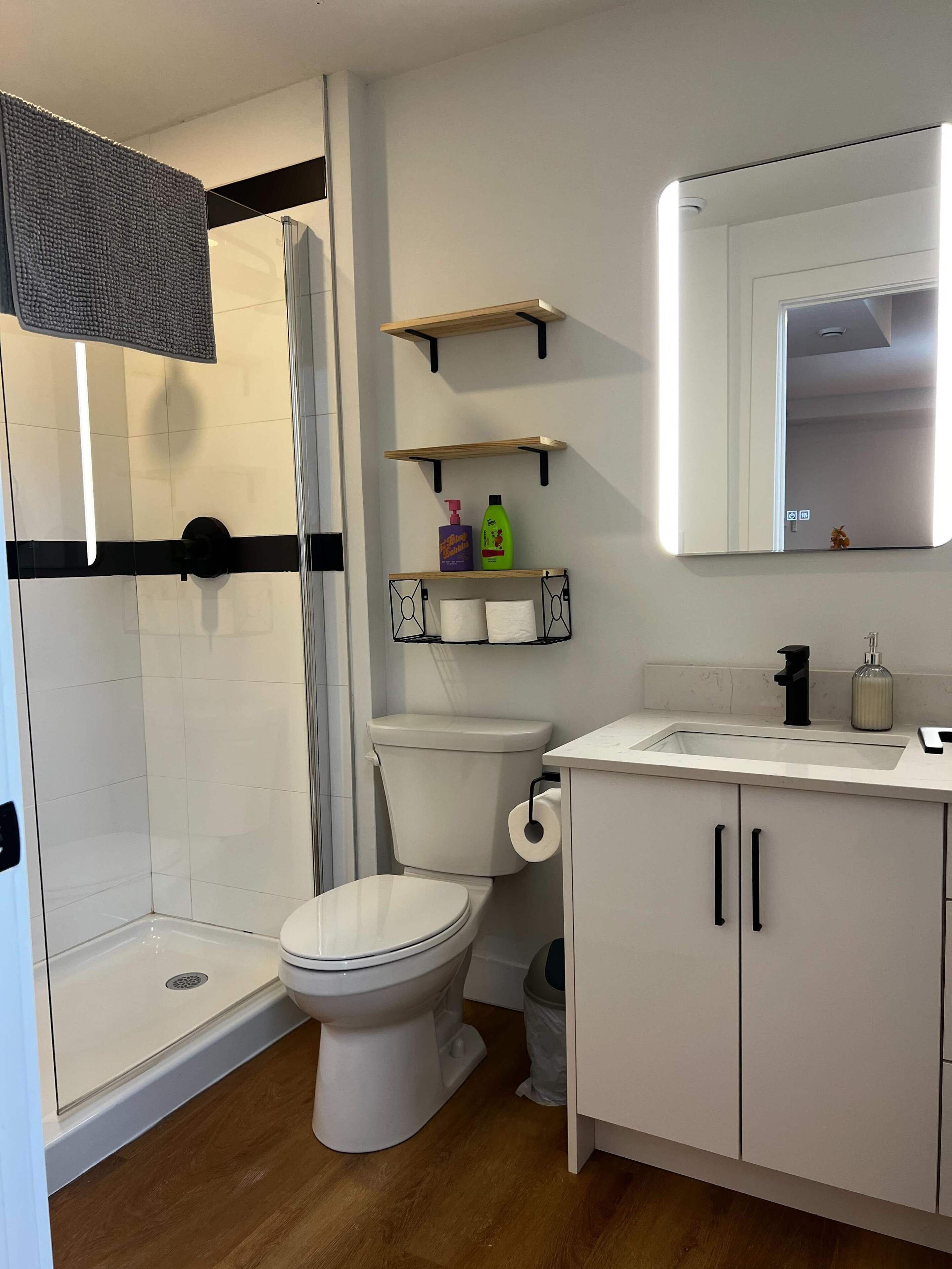 Une salle de bain moderne équipée d’une douche, de toilettes et d’un lavabo, avec des éléments en blanc et des touches de bois.