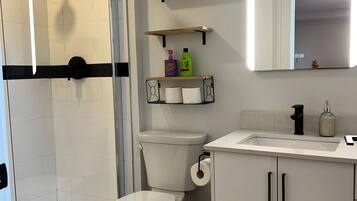 Une salle de bain moderne équipée d’une douche, de toilettes et d’un lavabo, avec des éléments en blanc et des touches de bois.