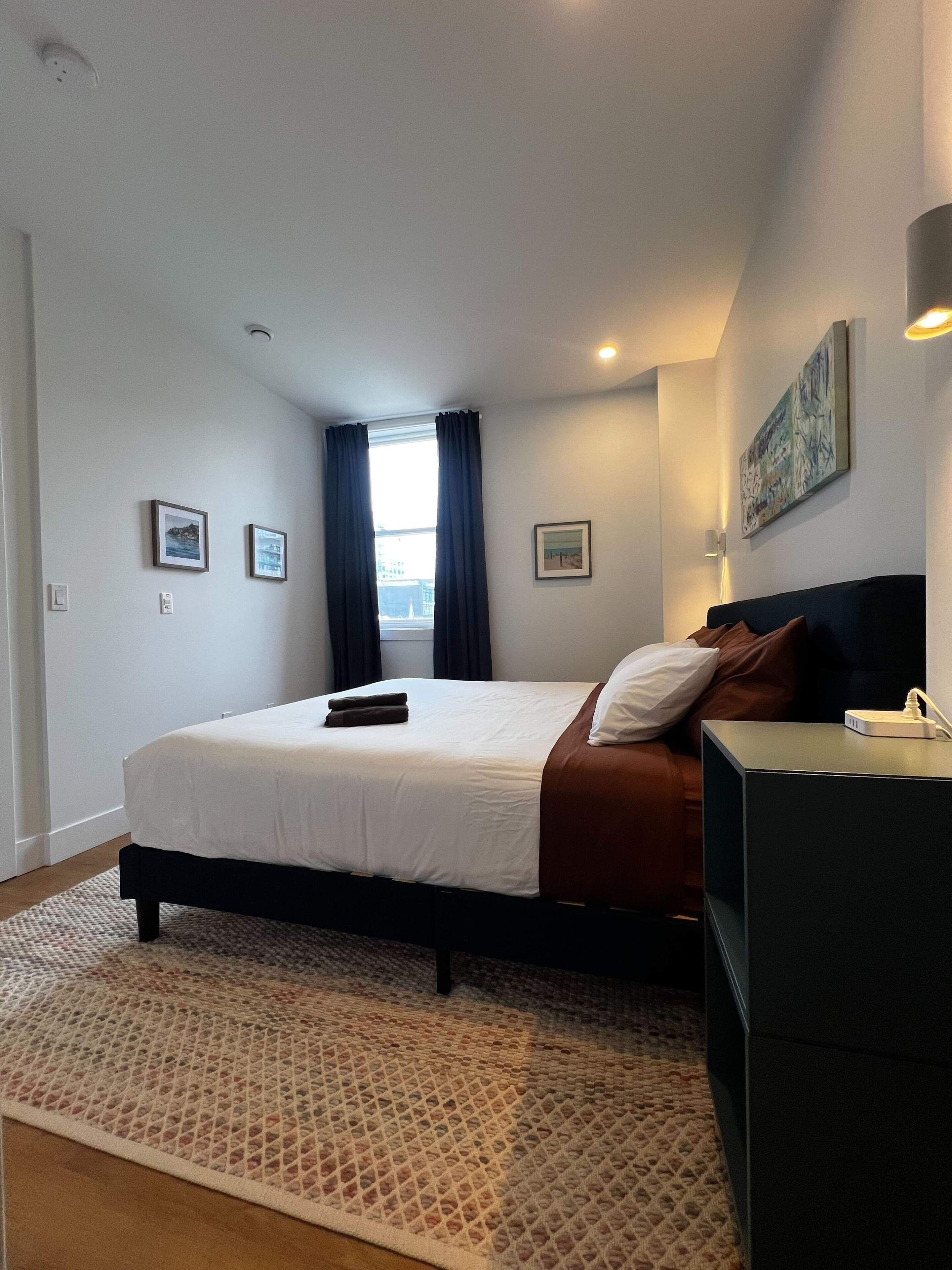 Une chambre d’hôtel avec un lit, un bureau, une fenêtre avec des rideaux et un tableau au mur.