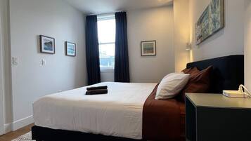 Une chambre d’hôtel avec un lit, un bureau, une fenêtre avec des rideaux et un tableau au mur.