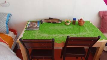 A room with a green lace tablecloth, two wooden chairs, a fish decoration, a Minecraft book, a basket of snacks, a bottle, and a clay pot.