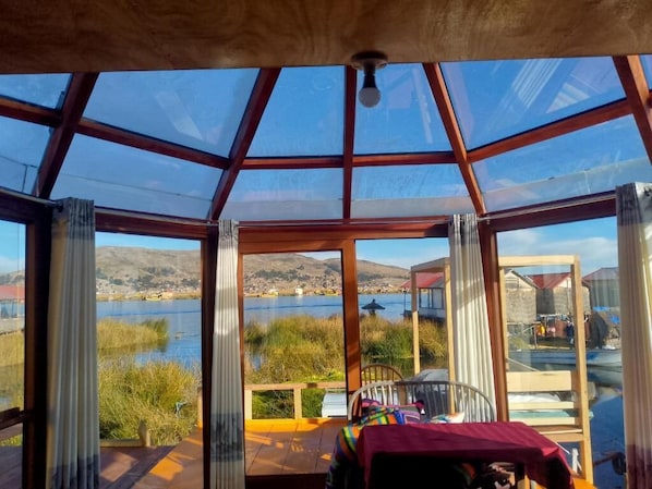 A room with a large glass ceiling, wooden beams, and a view of a lake and hills.