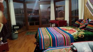 Una stanza con un letto grande, un tavolino e vista panoramica tramite una porta vetrata.