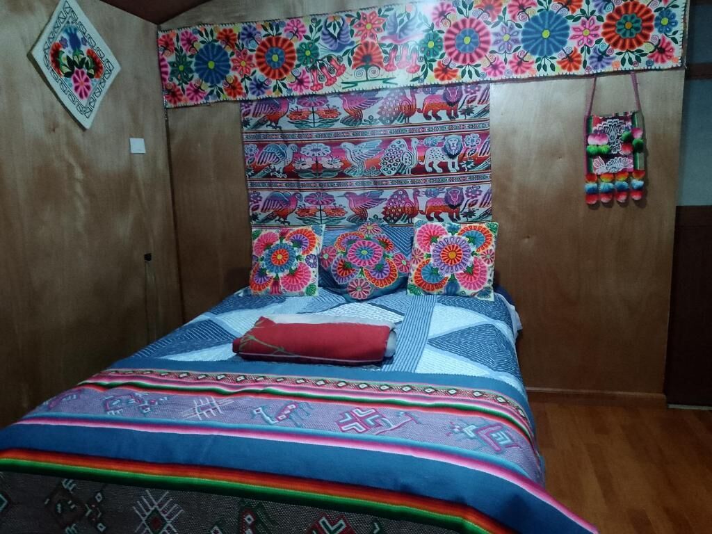 A room with a wooden headboard, a bed with colorful bedding, and a wall decorated with a floral pattern.