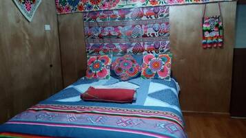 A room with a wooden headboard, a bed with colorful bedding, and a wall decorated with a floral pattern.