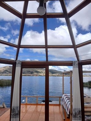 A room with a view of a lake and mountains, a bed with striped bedding, and a wooden floor.