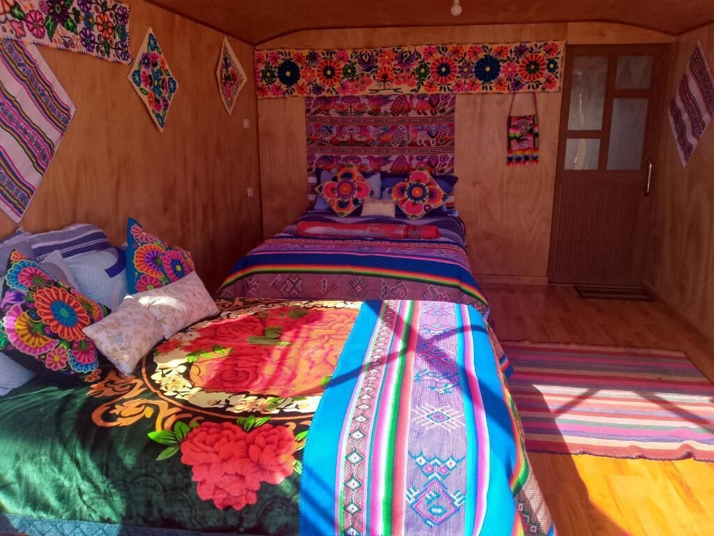 A room with a bed, wooden walls, and colorful wall hangings.