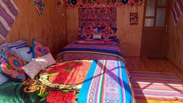 A room with a bed, wooden walls, and colorful wall hangings.