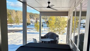 Ein überdachter Außenbereich mit Whirlpool, Tisch und Stühlen sowie Blick auf eine verschneite Landschaft.