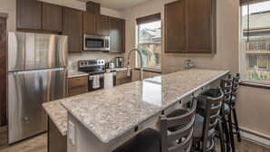 A kitchen with a central island, stainless steel appliances, and dark wooden cabinets. - NEW! Town Center Basecamp at Big Sky | Walk to Dining, Shops & Events | Prime Location (Big Sky)