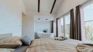 A modern hotel room with a large bed, a built-in bathtub, and a balcony with curtains.