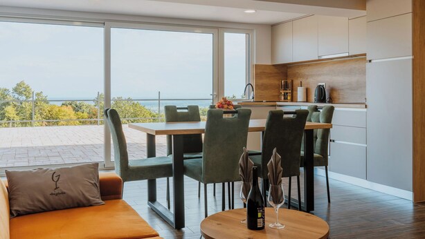 A modern kitchen with a dining area, large windows, and a view of the outdoors.