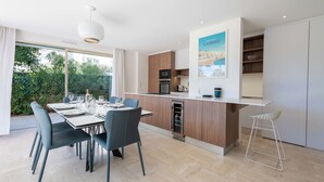 A modern kitchen with a dining area, wooden cabinets, and a view of greenery outside. - 3-Br Garden-Level Apartment – Near Beach with Parking (Cannes)