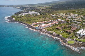 An aerial view of a coastal resort with multiple buildings, a swimming pool, and a rocky shoreline. - Hale Kai at Kona Isle (Kailua Kona)