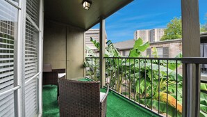 Un balcon agrémenté d’un revêtement de sol en gazon synthétique, de meubles en osier et offrant une vue sur les bâtiments et la verdure.