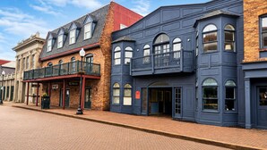 Une rangée d’immeubles en briques, présentant un mélange de styles architecturaux, dont un bâtiment doté d’un balcon et un autre avec une grande fenêtre en arc de cercle.