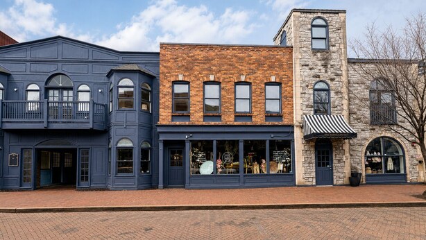 Une rangée d’immeubles à trois étages, dont les façades sont faites d’un mélange de briques et de pierres, avec de grandes fenêtres et une rue pavée de briques.