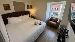 Une chambre d’hôtel avec un grand lit, une petite table avec une lampe, une fenêtre donnant sur des immeubles et une chaise.