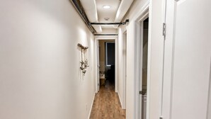 Un couloir avec un plancher en bois, des murs blancs et une porte sur le côté droit.