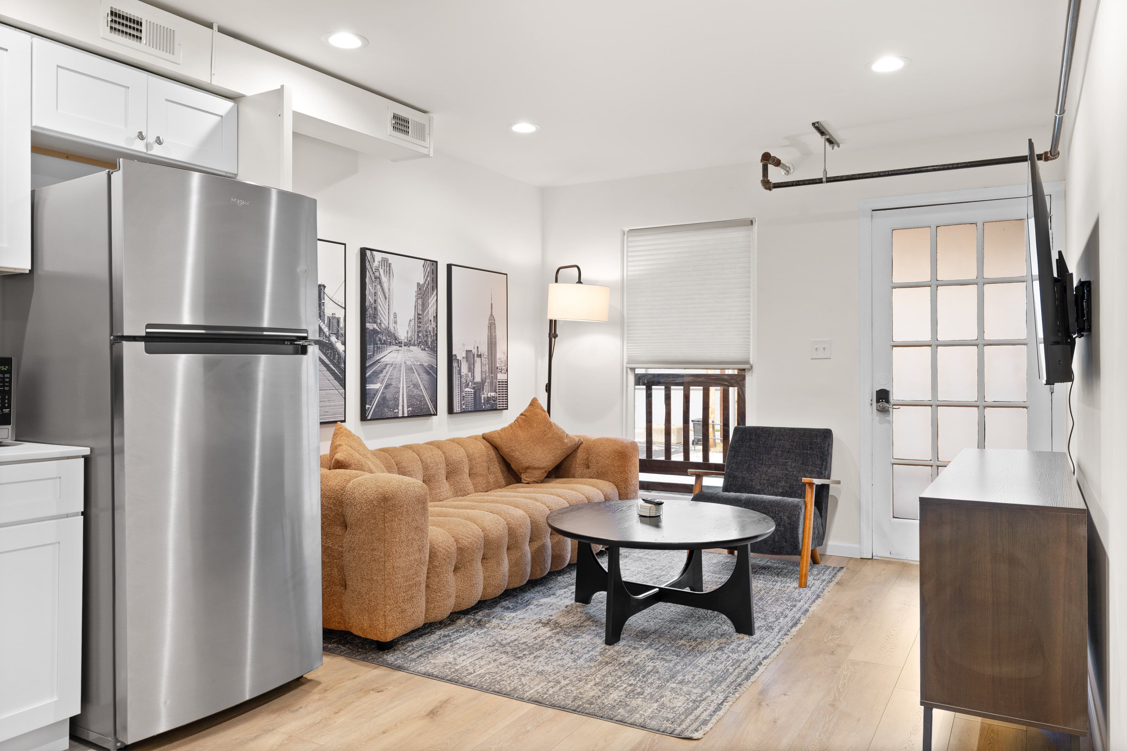 Bright living room with a tan sofa, round coffee table, and white kitchenette.