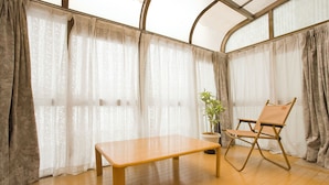 A room with a wooden floor, a wooden table, a folding chair, a potted plant, and sheer curtains. - [Sapporo Private House ] 8-minute walk from subway station and airport bus stop (Sapporo)