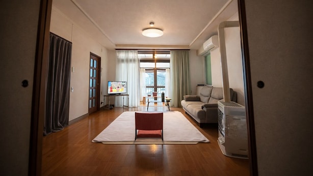 A modern living room with a flat-screen TV, a sofa, a coffee table, and a large window with curtains. - [Sapporo Private House ] 8-minute walk from subway station and airport bus stop (Sapporo)