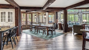 Un comedor amplio con una gran mesa y sillas de madera, una cocina con un armario blanco y vistas a través de ventanas grandes.