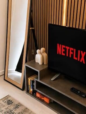 Un televisor con el logotipo de Netflix, un control remoto y un pequeño estante con objetos decorativos.