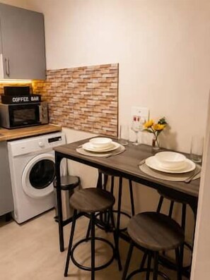 A compact kitchen with a coffee machine, a washing machine, and a small dining area with stools. - Flat in Manchester – Dudley's Dove (Manchester)
