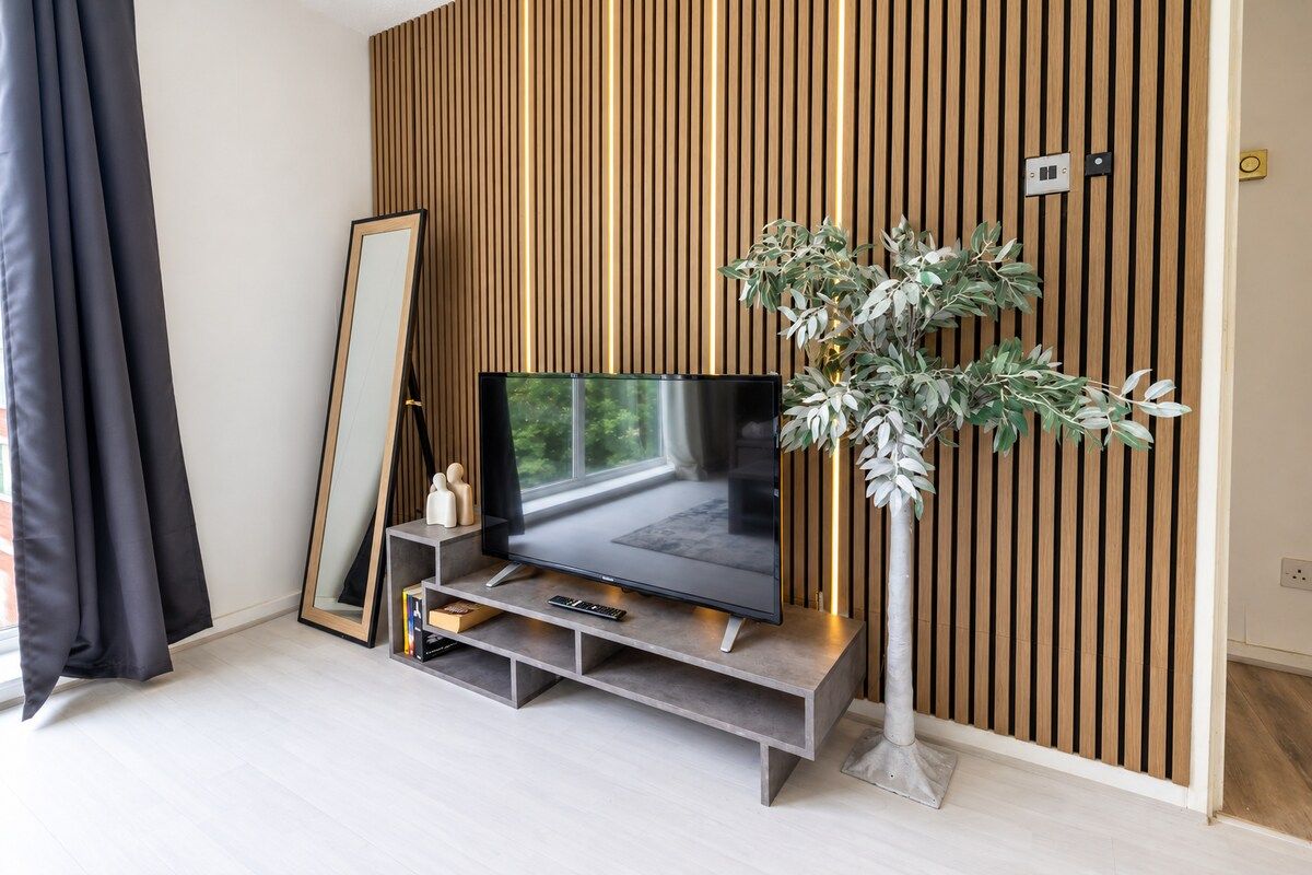 Un salon moderne avec un téléviseur à écran plat posé sur un meuble, un grand miroir et une plante en pot.