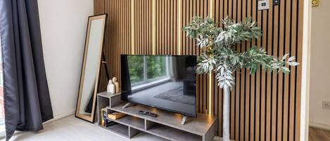 A modern living room with a flat-screen TV on a stand, a large mirror, and a potted plant.