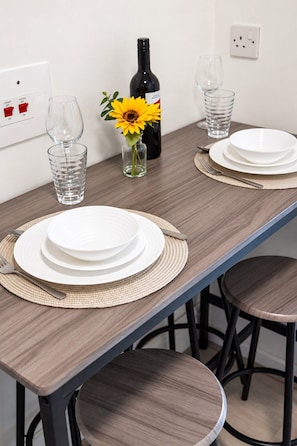 A dining table set with plates, cutlery, and glasses, with a bottle and a sunflower in a vase. - Flat in Manchester – Dudley's Dove (Manchester)