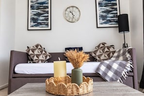A living room with a sofa, a coffee table with a candle and a vase, and a wall clock. - Flat in Manchester – Dudley's Dove (Manchester)