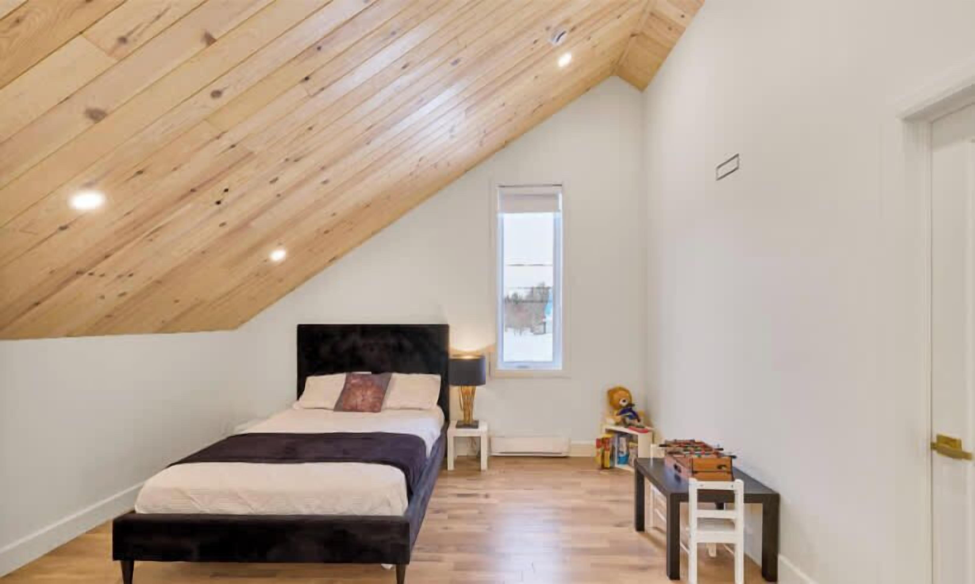 A bedroom with a sloped ceiling, a bed, a nightstand, a window, and a small table with toys.
