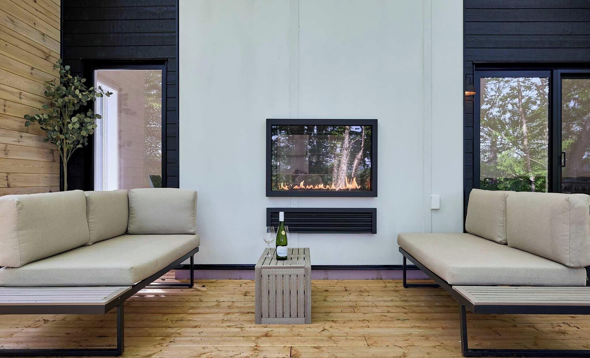 Een moderne woonkamer met twee banken, een klein houten tafeltje met een fles en glas, en een in de muur ingebouwde open haard.