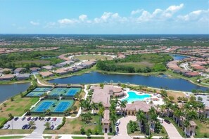 An aerial view of a residential area with a large swimming pool, tennis courts, and a lake. - Spacious 4-bedroom house in tranquil Venice with private lanai. (Venice)