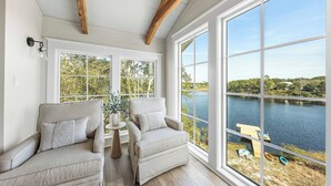 A room with two armchairs, a small table, and large windows overlooking a lake. - Bella Vista & Coastal Chateau: Lakefront Retreat with Dock, Kayaks, Bikes & Fire Pit (Seacrest)