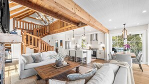 A spacious living area with a wooden staircase, a dining table, and a kitchen in the background. - Bella Vista & Coastal Chateau: Lakefront Retreat with Dock, Kayaks, Bikes & Fire Pit (Seacrest)
