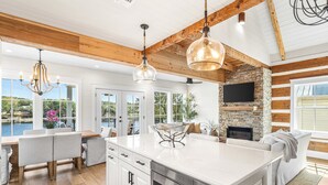 A spacious kitchen with a large island, wooden beams, a stone fireplace, and a view of the outdoors. - Bella Vista & Coastal Chateau: Lakefront Retreat with Dock, Kayaks, Bikes & Fire Pit (Seacrest)