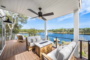 A covered deck with a ceiling fan, wooden furniture, and a view of a lake.