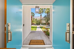 A doorway leading to a well-maintained outdoor area with a welcome mat, palm trees, and a clear view of mountains in the distance. - The White House Private Palm Springs Retreat (Palm Springs)