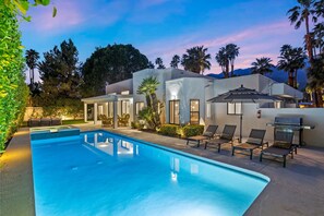 A swimming pool with lounge chairs, a barbecue grill, and a building with multiple windows and doors. - The White House Private Palm Springs Retreat (Palm Springs)