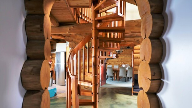 A spiral staircase in a log cabin interior with a view of a dining area. - Stunning Tidal Waters Loglodge (Tolaga Bay)